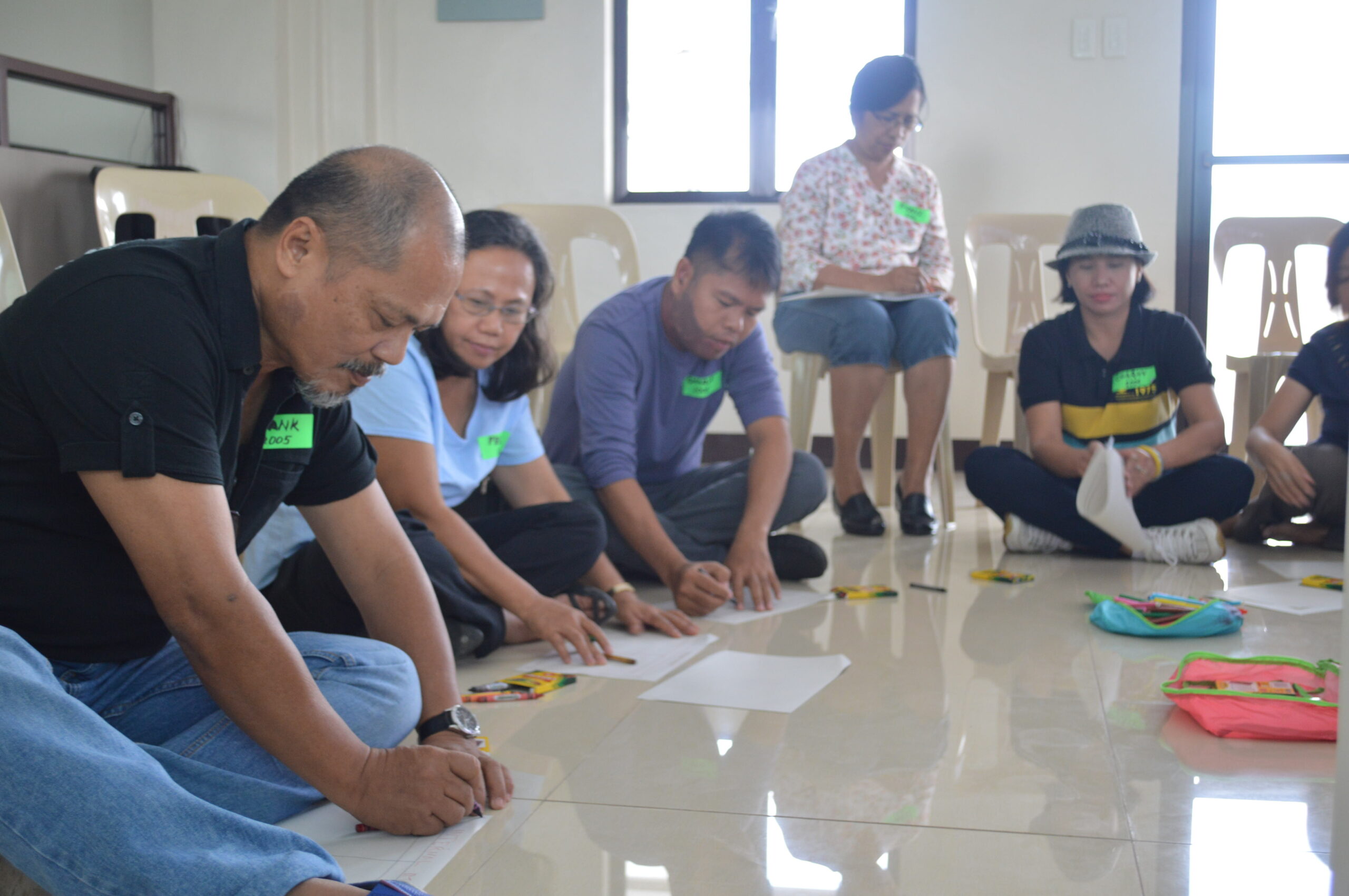 Filipino focus group participants seated on the floor, writing.